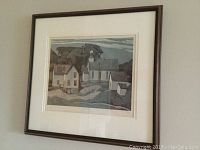 Framed print of stylized houses and a church in muted tones, isolated against a plain wall, showing the whole artwork and frame.