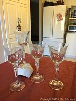 Photo of four clear wine glasses with etched floral designs on a red cloth surface in a kitchen setting