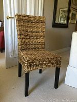 Single wicker chair with woven natural fibers and dark wooden legs placed indoors against a wall.