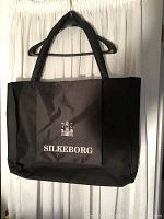 Photo of the black Silkeborg folio bag hanging on a hanger showing front side with logo.