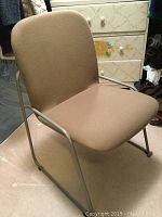 Beige modern chair with cushioned seat and backrest and metal tubular frame with armrests.