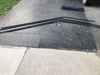 Metal tent frame poles laid on paved ground along with stakes and connectors in plastic bag