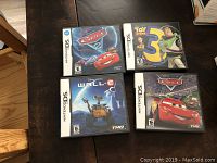 Photo showing four Nintendo DS game cases: Cars 2, Toy Story 3, Wall-E, and Cars arranged on table.