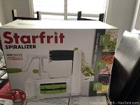 Front view of Starfrit Spiralizer box showing the product in white and green, with hand crank and spiralized vegetable.