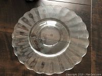 Photo shows a clear glass serving dish with scalloped edges on a dark surface. The dish has a circular indentation in the center for serving purposes.