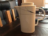 Front view of the white Mikasa Caviar teapot showing its cylindrical shape, handle, spout, and black line design.