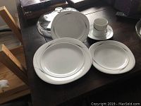 Photo of the Mikasa Caviar place setting including coffee cup, saucer, dinner plate, salad plate, and soup bowl with lid arranged on a wooden table.