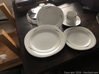 Photo of Mikasa Caviar place setting including coffee cup, saucer, dinner plate, salad plate, and soup bowl with a silver/platinum band on white ceramic.