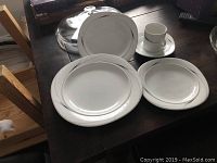 Photo showing Mikasa Caviar place setting pieces arranged on a table: coffee cup, saucer, dinner plate, salad plate, and soup bowl, all white with silver trim.