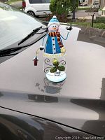 Front view of the metal snowman tea light holder Christmas decoration on a car hood.