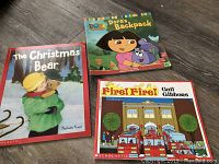 Photo showing three children's books: 'Dora's Backpack', 'The Christmas Bear', and 'Fire! Fire!'.