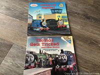 Photo showing two soft cover Thomas the Train children's books: "Calling All Engines!" and "Thomas Gets Tricked and Other Stories".
