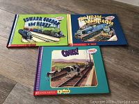 Three Thomas The Train hardcover books titled 'Edward, Gordon and Henry', 'Paint Pots and The Royal Queen', and 'Cows!' displayed on wood floor.
