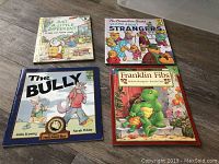 Photo of four children's books: Just a Little Different, The Berenstain Bears Learn About Strangers, The Bully, Franklin Fibs, arranged on wooden floor.