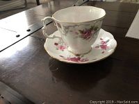 Tea cup and saucer placed on a dark wooden surface showing the floral design and gold trim.