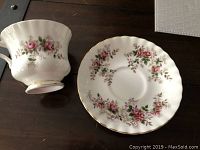Tea cup and matching saucer laid flat on a dark wooden surface showing floral decoration and gold trim.