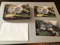 Box of Thomas Kinkade note cards with two different card designs and white envelopes laid out on a table.