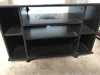 Front view of the black TV stand showing internal shelves and compartments, used condition with visible wear marks.