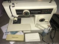 Kenmore 10-stitch sewing machine with stitch selector and partially visible accessories including instruction manual and boxes.