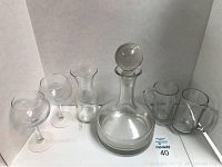 Clear glass barware including a decanter, two cocktail glasses, a small carafe, and two mugs.
