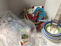 Clear plastic crystal look serving bowls and trays stacked with ceramic bowls and small glasses on right corner.