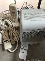 Photo showing MaxHeat ceramic heater with caution label, white extension cords and Uniden cordless phone handset and base, all together coiled with cords.