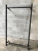 Black metal twin bed rails standing against a concrete wall