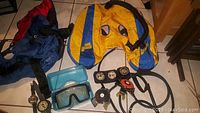 Photo of scuba gear laid out on floor showing SeaQuest BC pack, dive mask, gauges, and hoses