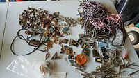Wide view of assorted stone pendants, metal jewelry components, cords, and other bolo tie/craft making parts displayed on table.
