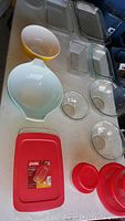 Photo showing various clear glass Pyrex bowls, yellow and pale blue mixing bowls, rectangular baking dishes, and several red plastic lids on a white table.