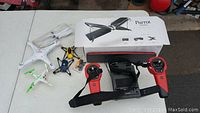 Overview of drone parts including Parrot Swing drone box, white quadcopter, smaller yellow and blue quadcopters, and red and black Skycontroller with straps