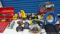 Wide view of power tools including circular saw, cordless drills, batteries, and air compressor.