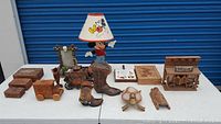 Photo showing entire lot on white table including vintage Mickey Mouse lamp, wooden carved boxes, cowboy boots, toy truck bank, carriage figurine, pottery and other decorative pieces