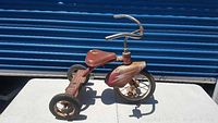 Side view of the antique red metal children's tricycle showing rust and wear.