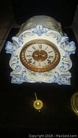 Front view of the porcelain mantle clock with floral design and open glass door showing Roman numeral dial and gold bezel.