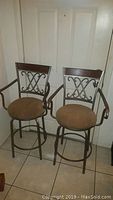 Two matching metal frame bar stools with decorative backrests and brown cushioned seats placed side by side.
