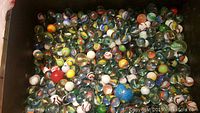 Top-down view of a box filled with over 400 assorted glass marbles in multiple colors, sizes, and swirl patterns.
