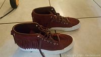 Side and top view of brown suede Vans moccasin-style high top shoe with fringe and white rubber sole.