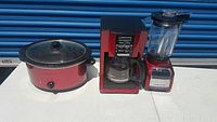 Photo showing all three items: red crock pot with glass lid, red blender with glass pitcher, and red coffee maker with glass carafe and control panel.