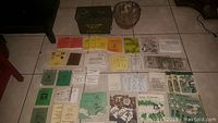 Photo showing an array of pocket training manuals in multiple colors arranged alongside a green military ammo box and a rusted helmet.