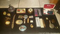 Top view of all items displayed on a black surface showing pens, buckles, lighters, barometer, a decorative disk, and other small collectibles.
