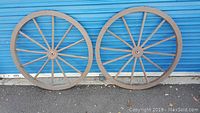 Two large wooden wagon wheels side by side against a blue door, showing overall size and structure