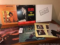 Photo of several vinyl record album covers including Arlo Guthrie's "Alice's Restaurant", Elvis Presley's "Back In Memphis", Genesis "Three Sides Live", Climax Blues Band and others.
