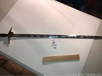 Full-length view of the sword laid flat with a wooden scabbard or display block beside it