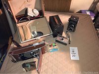Wide view showing all cameras, flashbulbs, and camera case laid out on surface with seller tag
