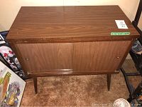 Full view of vintage wood cabinet with sliding doors, showing top surface and legs. Wear visible on edges.
