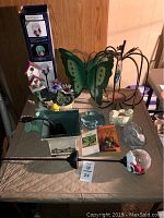 Photo showing full view of gardening lot items including boxed Moonrays solar cardinal lamp, green metal butterfly, birdhouses, flower pot, garden statues, and gardening books on a table.