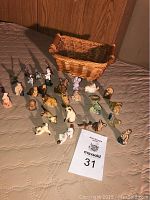 Thirty miniature Wade figurines on mattress near wicker basket with MaxSold lot number sheet