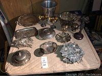 Overview of silver plated items spread on a table including trays, bowls, goblets, and trivets.