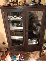 Front view of the vintage dark brown wood china cabinet showing glass-paneled double doors, wooden frame, and a drawer at the bottom.